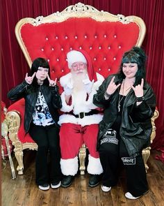 three people dressed as santa clause sitting on a red chair