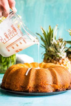 someone pouring milk on top of a bundt cake with pineapples in the background