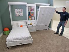 a man standing next to a bed in a room with two white bookcases