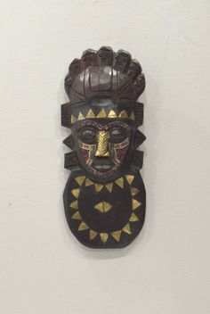 a wooden mask hanging on the wall with gold and black decorations around it's face