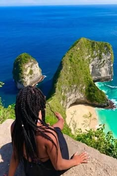 a woman sitting on top of a cliff next to the ocean with two cliffs in the background