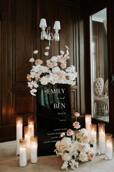 a table topped with lots of white flowers and lit candles next to a black sign