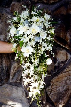 a bouquet of white flowers sitting on top of a stone wall next to a person's hand