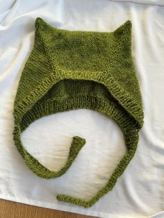 a green knitted cat hat laying on top of a white bed sheet and pillow