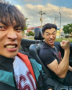 two men sitting in the back seat of a car, one with his fist raised