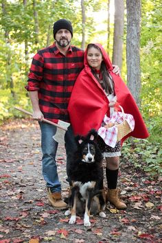 a man and woman standing next to a black and white dog in the woods under a red blanket