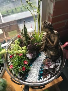 a buddha statue sitting on top of a metal bowl filled with plants