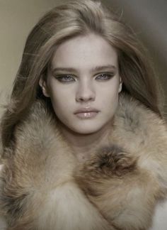 a woman with long hair and blue eyes wearing a fur stole around her neck is looking at the camera