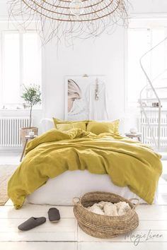 a bed with yellow sheets and pillows in a white room next to a wicker basket