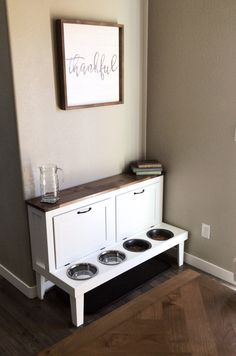 a white dog house with three bowls on the bottom shelf and a sign above it