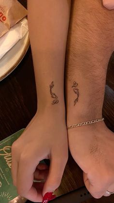 two people with matching tattoos on their arms, one is holding a knife and the other has a book