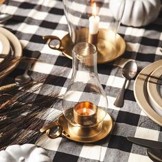 a black and white checkered table cloth with gold candlesticks, plates and silverware