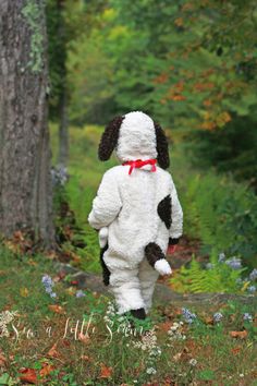 a stuffed dog that is walking in the grass with trees and flowers behind it,