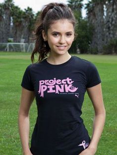 a girl in a black t - shirt is standing on the grass with her hands in her pockets