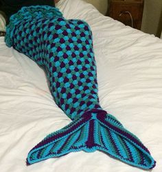 a crocheted mermaid tail laying on top of a bed next to a pillow