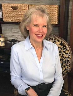 an older woman sitting in a chair with her hands on her hips and smiling at the camera