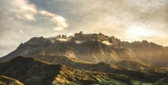 the mountains are covered in green grass and clouds as the sun is setting over them