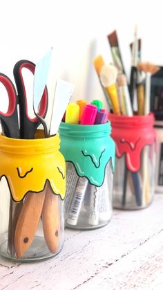 three mason jars with pens, scissors and pencils in them sitting on a table