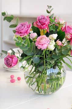 a vase filled with lots of pink roses on top of a white table next to confetti