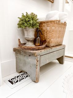 an old wooden bench with baskets and towels on it, next to a potted plant