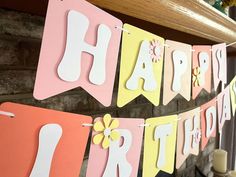 a happy birthday banner hanging from a fireplace with candles and flowers on the mantel