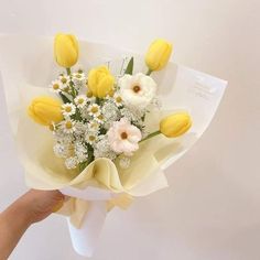 a bouquet of yellow and white flowers is being held by a person's hand