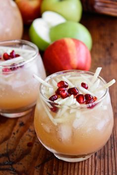 two glasses filled with drinks sitting on top of a wooden table next to some apples