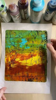 someone is holding up an art piece with some paint and watercolors on it