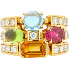 Discover the epitome of elegance and artistry with the 18K Yellow Gold BVLGARI Allegra 3 Ring Band. This exquisite piece is a celebration of vibrant colors and dazzling brilliance, meticulously crafted to capture the essence of sophistication. The ring features a harmonious blend of gemstones: a captivating blue cabochon, a verdant green gemstone, a radiant pink center stone, and a fiery orange gem, all set against the luxurious backdrop of 18K yellow gold. Each gemstone is securely held in plac Luxury Multi-stone Yellow Gemstones, Luxury Yellow Multi-stone Gemstones, Elegant Multicolor Brilliant Cut Gemstones, Formal Multicolor Diamond Gemstones, Luxury Multicolor Multi-stone Gemstones, Luxury Multicolor Gemstones With Accents, Formal Multicolor Fine Jewelry Gemstones, Multicolor Diamond Gemstones With Accents, Luxury Multicolor Gemstones