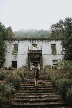 a person walking up some stairs in front of an old building with trees and bushes