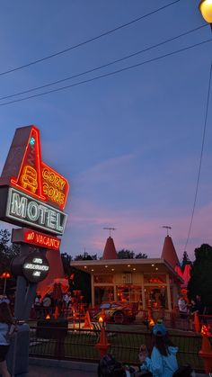 the neon motel sign is lit up at night with people sitting on benches around it