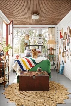 a dog sitting on top of a bed next to a trunk in the middle of a room