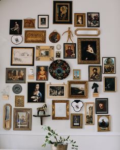 a wall with many framed pictures on it and a potted plant in the corner