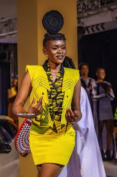 a woman is walking down the runway wearing a bright yellow dress and headpieces