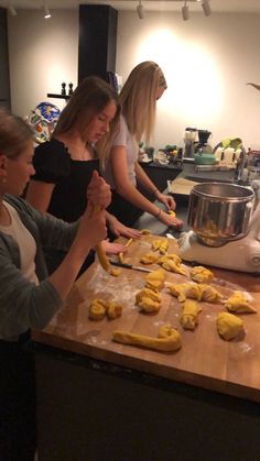 three women are making cookies on a counter top while another woman stands in the background