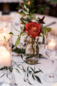 a table with candles and flowers in vases on top of the table is decorated with greenery