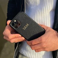 a person holding a black cell phone in their left hand and wearing a white shirt