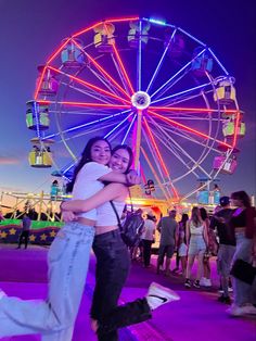 two people hugging each other in front of a ferris wheel at an amusement park during the night