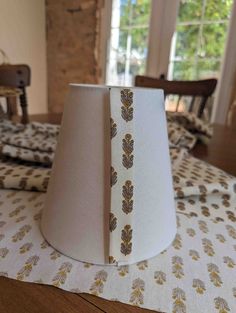 a white lamp shade with gold leaf print on the bottom and beige fabric around it