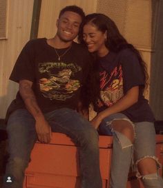 a man and woman sitting next to each other on top of an orange crate smiling at the camera