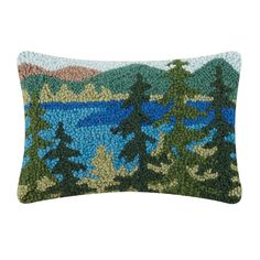 a blue and green pillow with trees in the background on a white surface, it is made out of knitted material