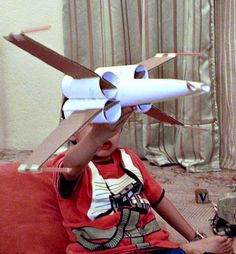 a young boy sitting on a couch with a paper airplane attached to his head and hands