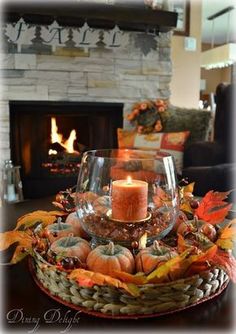 a candle is lit in a glass bowl filled with autumn leaves and pumpkins on a table