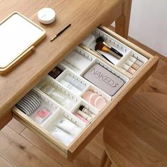 an open drawer on a wooden table with makeup and other items in the drawers next to it