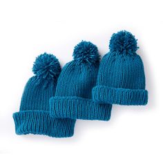 three blue knitted hats with pom - poms on them, sitting next to each other