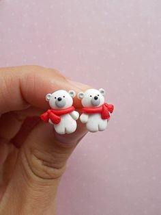 two small white teddy bears wearing red scarfs on their fingers, sitting in front of a pink wall