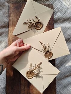 two envelopes with flowers and wax stamp on them are being held by a person's hand