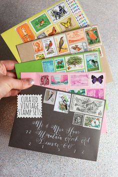 a hand holding a envelope with stamps on it next to a pile of other mail