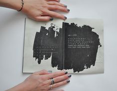 two hands holding an open book with black paint on the pages and writing in it