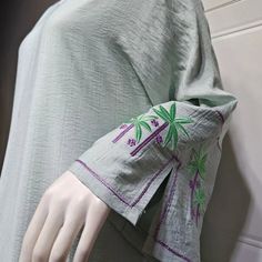 This open abaya is trending now and we know why! A light green stylish open abaya embroidered with green and purple palm trees on the sleeves, a low shoulder shrug stitching, stunning colors, breathable fabric, and button closures to take this from an open abaya to a closed abaya! Style up or down for an effortlessly classy look. Available in 2 colors and 5 sizes. Green Dress With Embroidered Sleeves For Eid, Green Embroidered Long Sleeve Abaya, Long Sleeve Abaya For Eid Vacation, Eid Vacation Long Sleeve Abaya, Green Long Sleeve Kaftan With Floral Embroidery, Long Sleeve Thobe For Eid Vacation, Long Sleeve Thobe For Vacation On Eid, Traditional Long Sleeve Abaya For Vacation, Embroidered Long Green Abaya